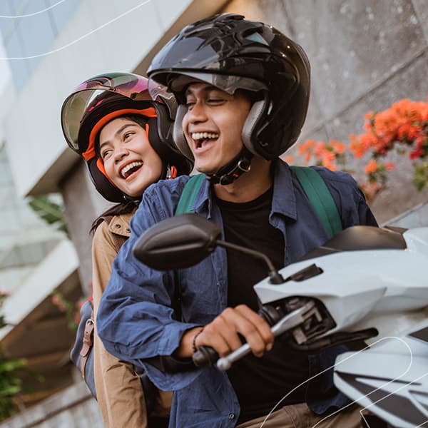 Simule e descubra os valores das parcelas do seu consórcio de motos Embracon Casal sorrindo em uma moto enquanto passeiam pela cidade