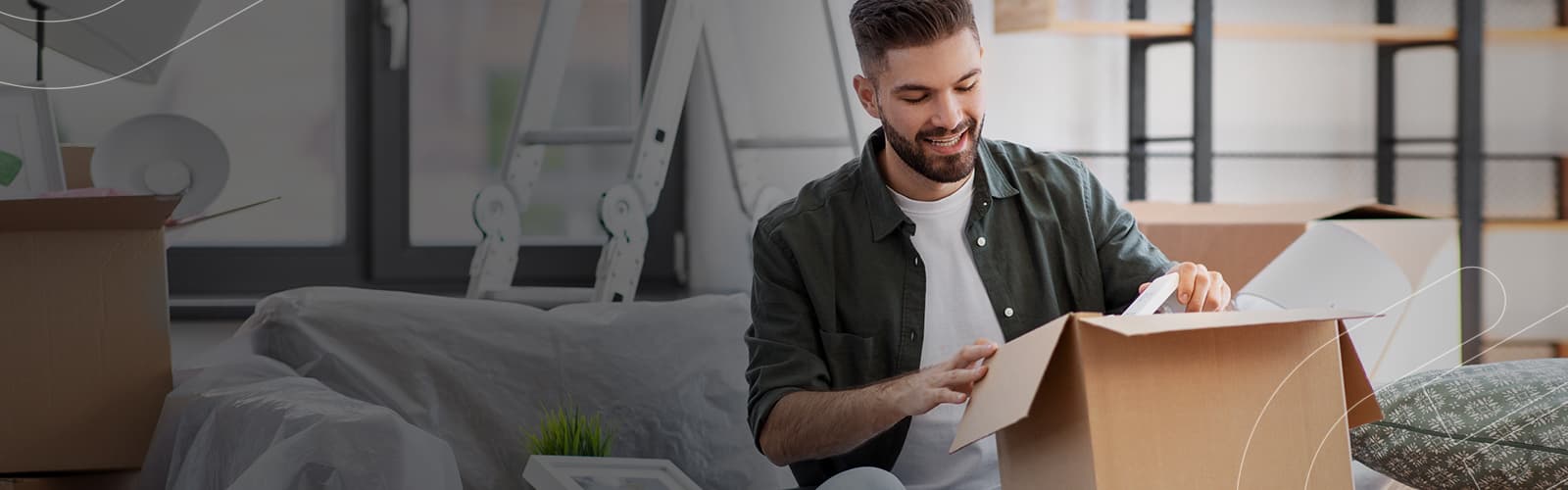 A conquista da sua casa própria está ao seu alcance com o consórcio de imóveis Embracon! Rapaz abrindo uma caixa de papelão dentro da sua casa nova comprada pelo consórcio Embracon