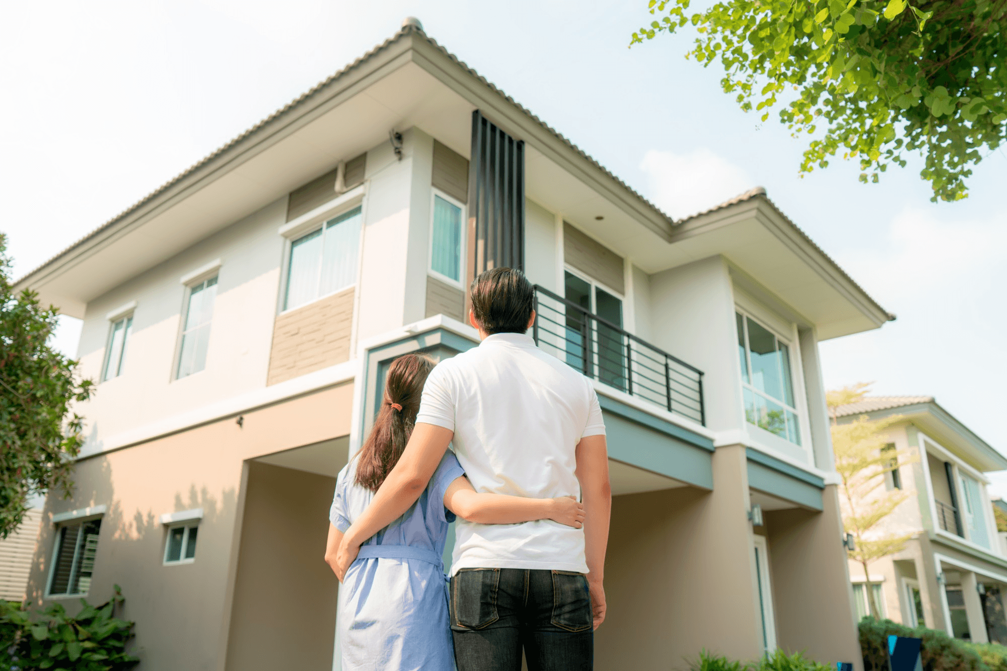Simule o consórcio imobiliário Embracon agora mesmo e dê o primeiro passo para a conquista da sua casa própria Casal se abraça observando sua casa nova de dois andares e linhas retas adquirida por meio do consórcio Embracon